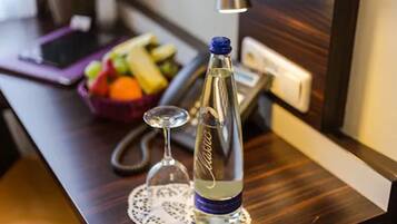 A bottle of water, a glass, and a fruit bowl on a wooden table.