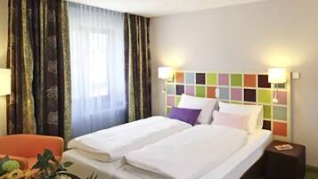 A hotel room with a double bed, two bedside tables, a nightstand, a lamp, a chair, and a window with curtains.