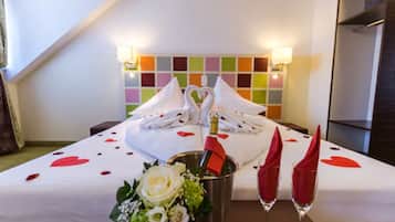 Une chambre d’hôtel avec un lit, un bouquet de fleurs, deux coupes à champagne et une bouteille de champagne.
