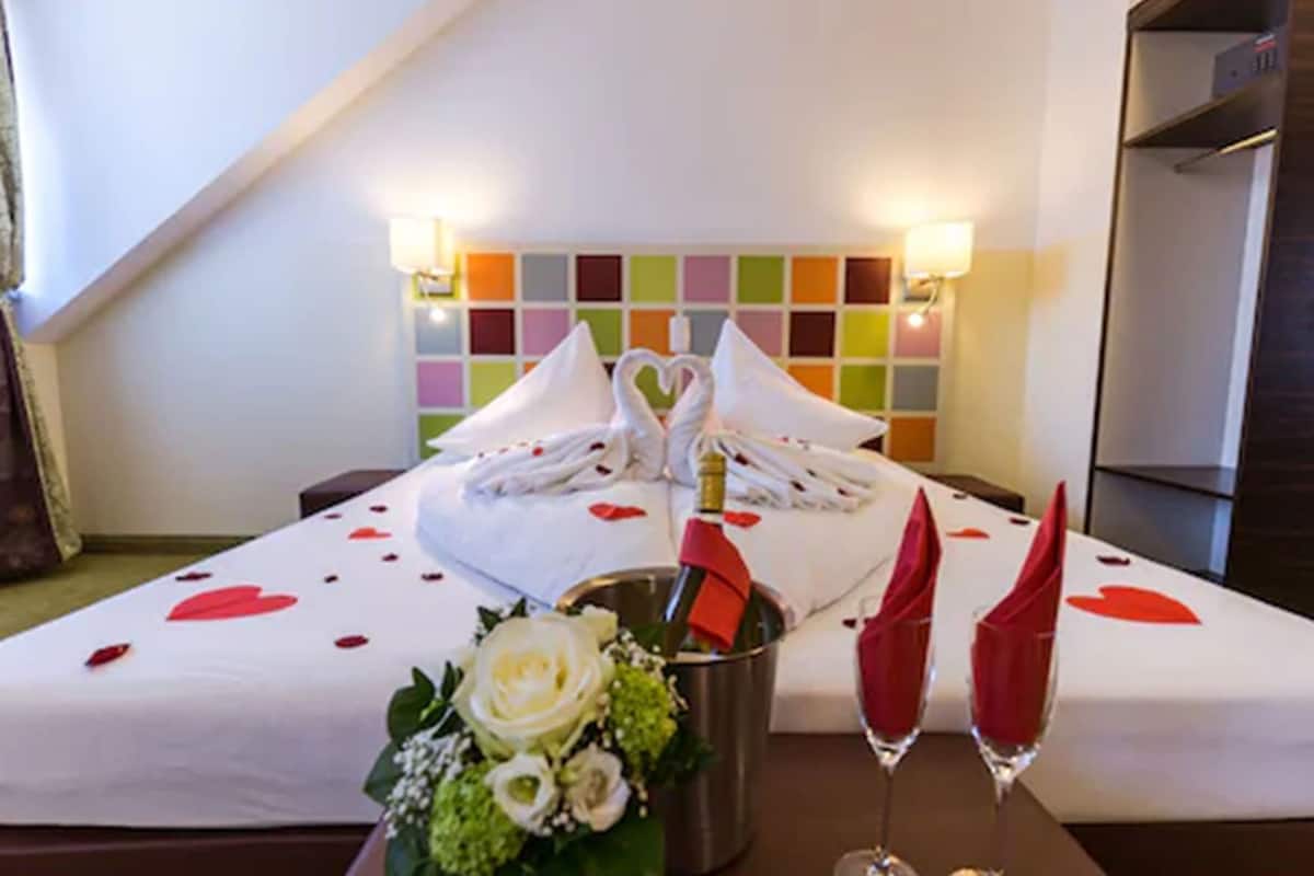 A hotel room with a bed, a bouquet of flowers, two champagne flutes, and a bottle of champagne.
