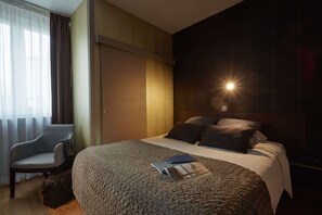 Una habitación de hotel con una cama grande, una silla, una mesita de noche y un tocador.