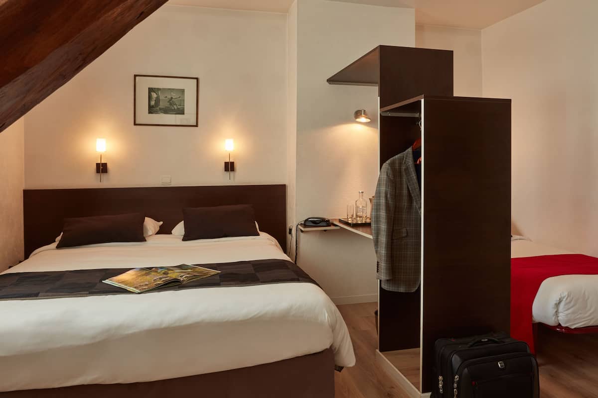 Habitación de hotel con una cama grande, un armario, una mesita de noche con lámpara y un cuadro en la pared.