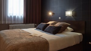 Una habitación de hotel moderna con una cama grande, paredes oscuras y una lámpara fijada a la pared.