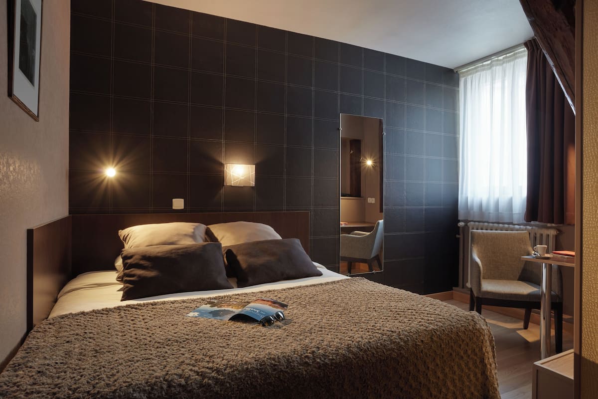 Una habitación de hotel con una cama grande, una silla, una mesita y un espejo.