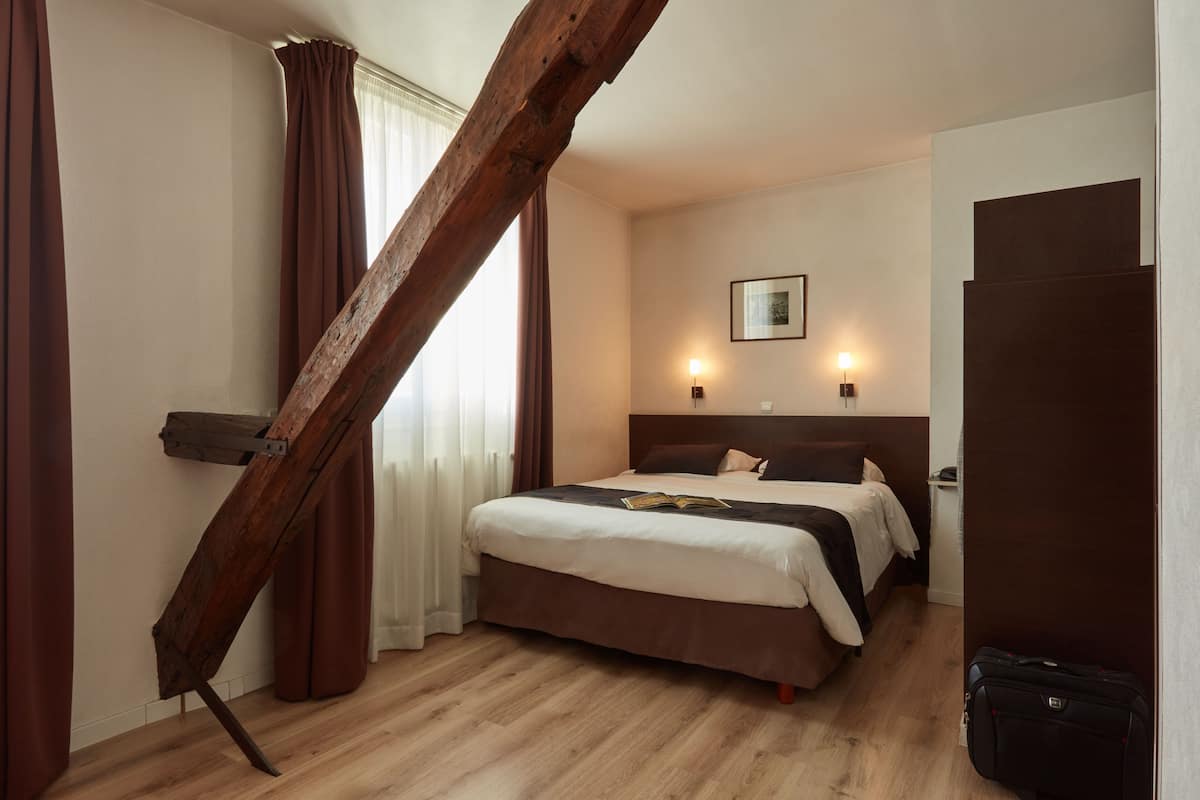 Habitación de hotel con escalera de madera, una cama con cabecera, dos lámparas de noche y suelo de madera.