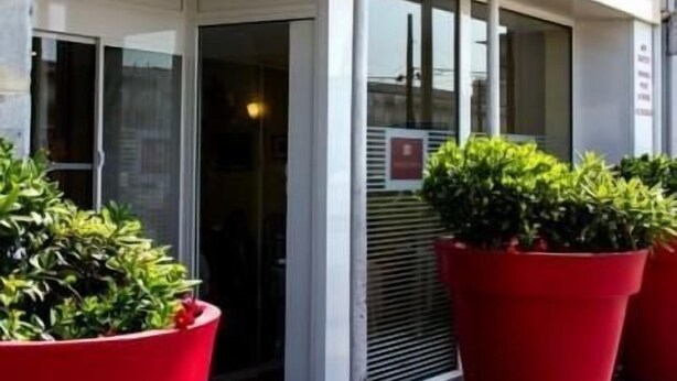 La entrada del Hotel Ashley, con un frente de vidrio transparente y plantas en macetas rojas al frente.
