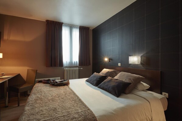 A modern hotel room with a large bed, a desk, and a window with curtains.