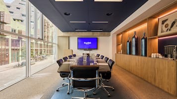A conference room with a large table, chairs, a TV screen, and a view of the street outside.