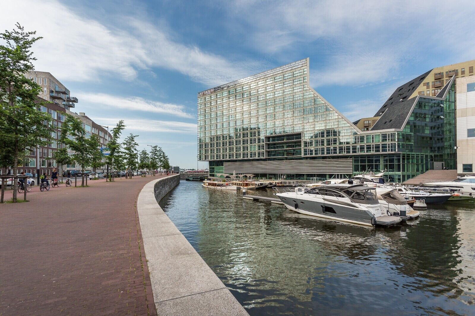 Ein modernes Gebäude mit Glasfassade, ein Kanal mit Booten und ein Fußweg.