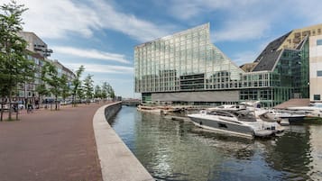 Ein modernes Gebäude mit Glasfassade, ein Kanal mit Booten und ein Fußweg.