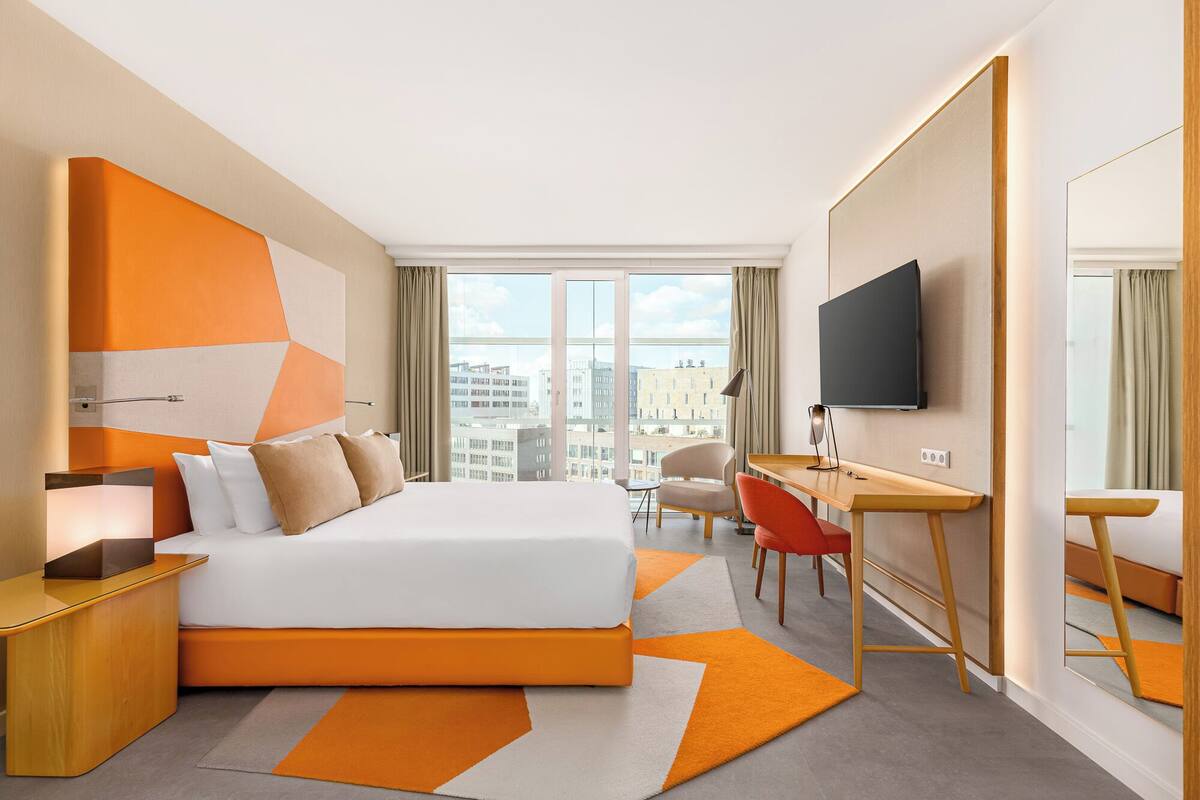 Habitación de hotel moderna con una cama grande, un escritorio, una silla y un televisor.