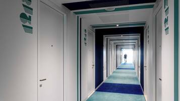 Un largo y estrecho pasillo de hotel con alfombra azul, paredes blancas y puertas a ambos lados.