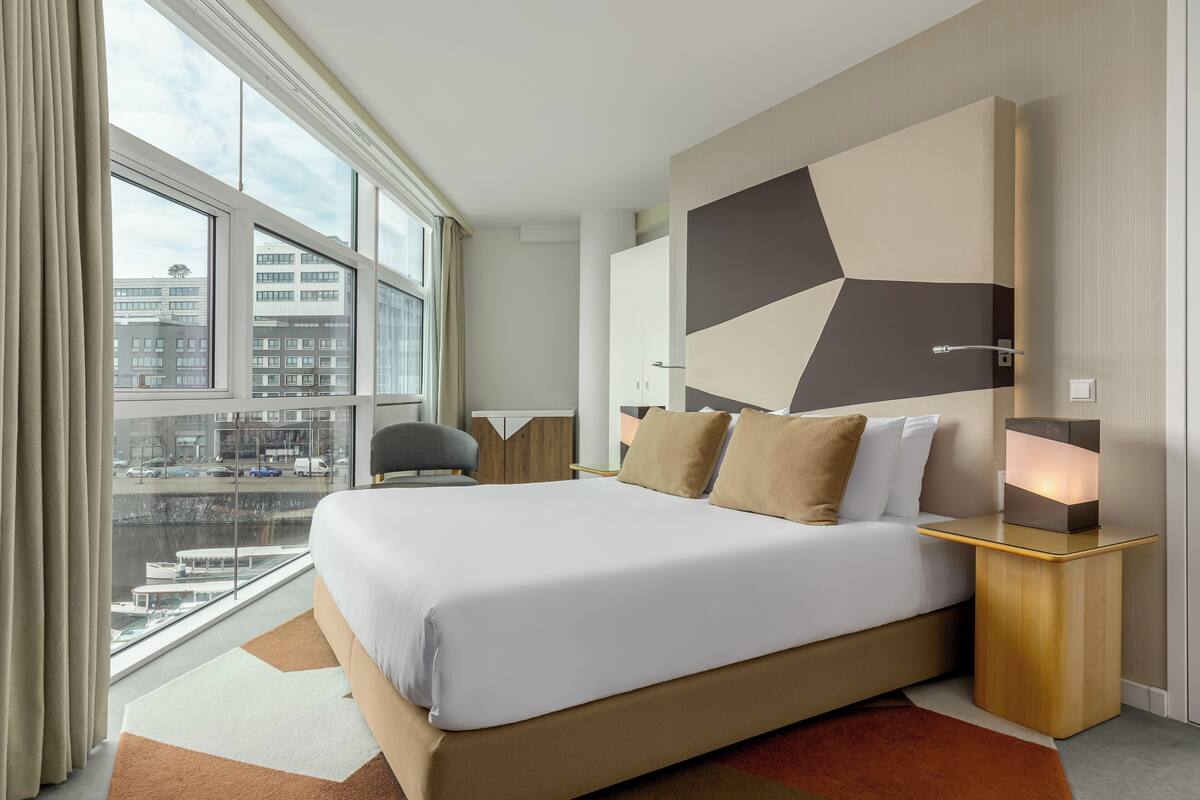 Una habitación de hotel moderna con una cama grande, vistas a la ciudad y un diseño geométrico en la pared.