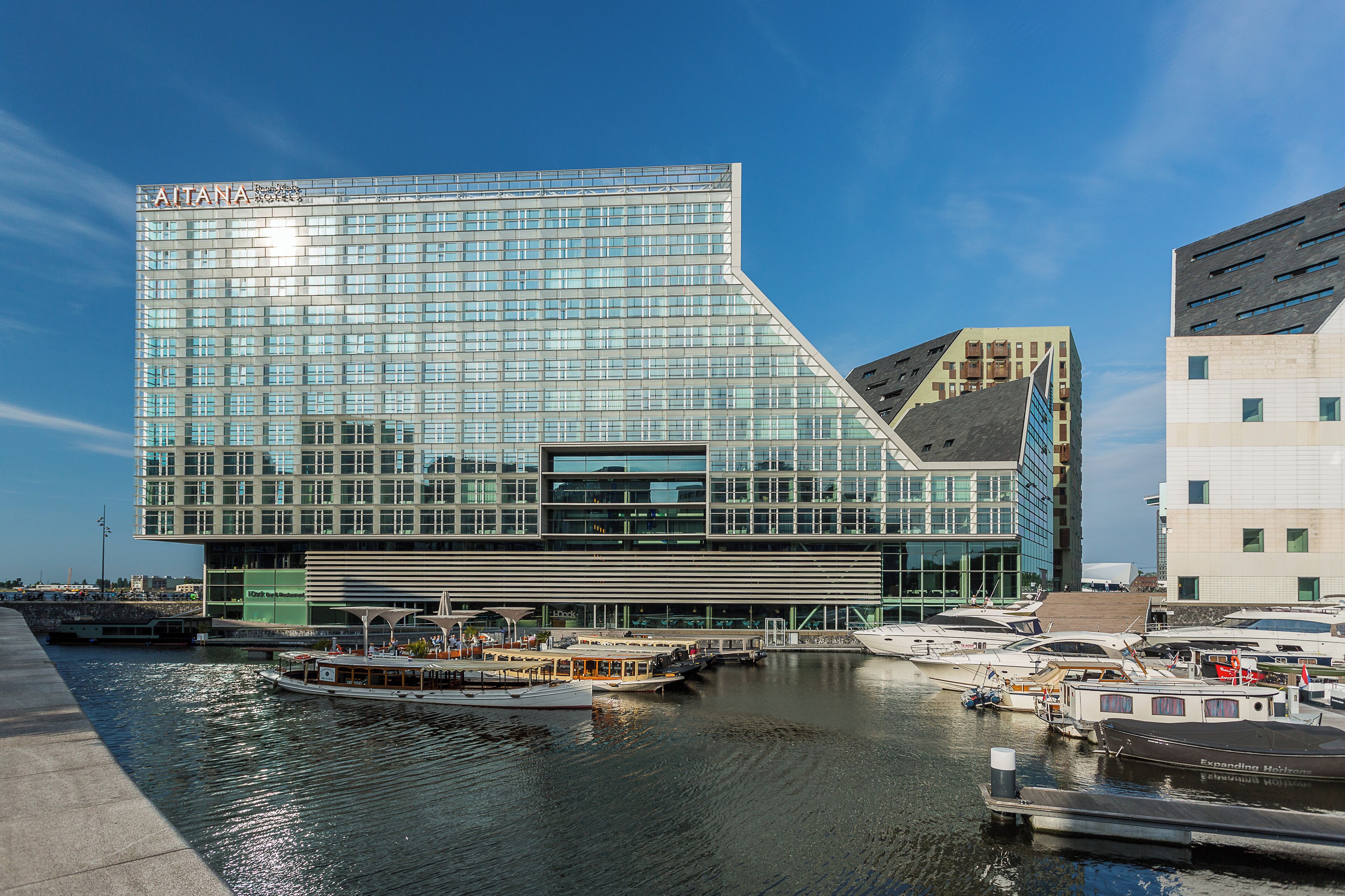 A modern building with a unique angular design, a waterfront location, and a marina with boats.