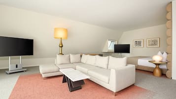 Une chambre d’hôtel moderne dotée d’un canapé d’angle, d’un téléviseur à écran plat, d’un bureau avec une lampe et d’œuvres d’art accrochées aux murs.