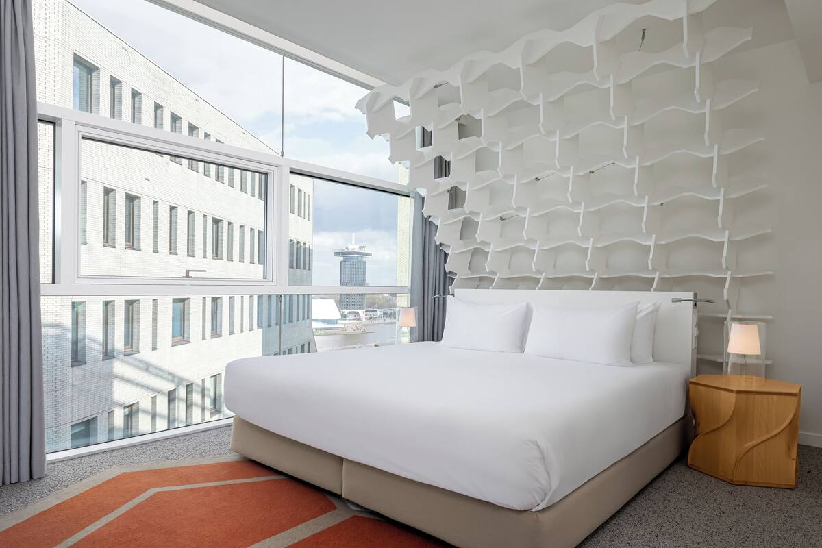 Habitación de hotel moderna con una cama grande, vistas a la ciudad y un diseño de pared original.