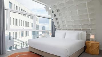 A modern hotel room with a large bed, a view of the cityscape, and a unique wall design.