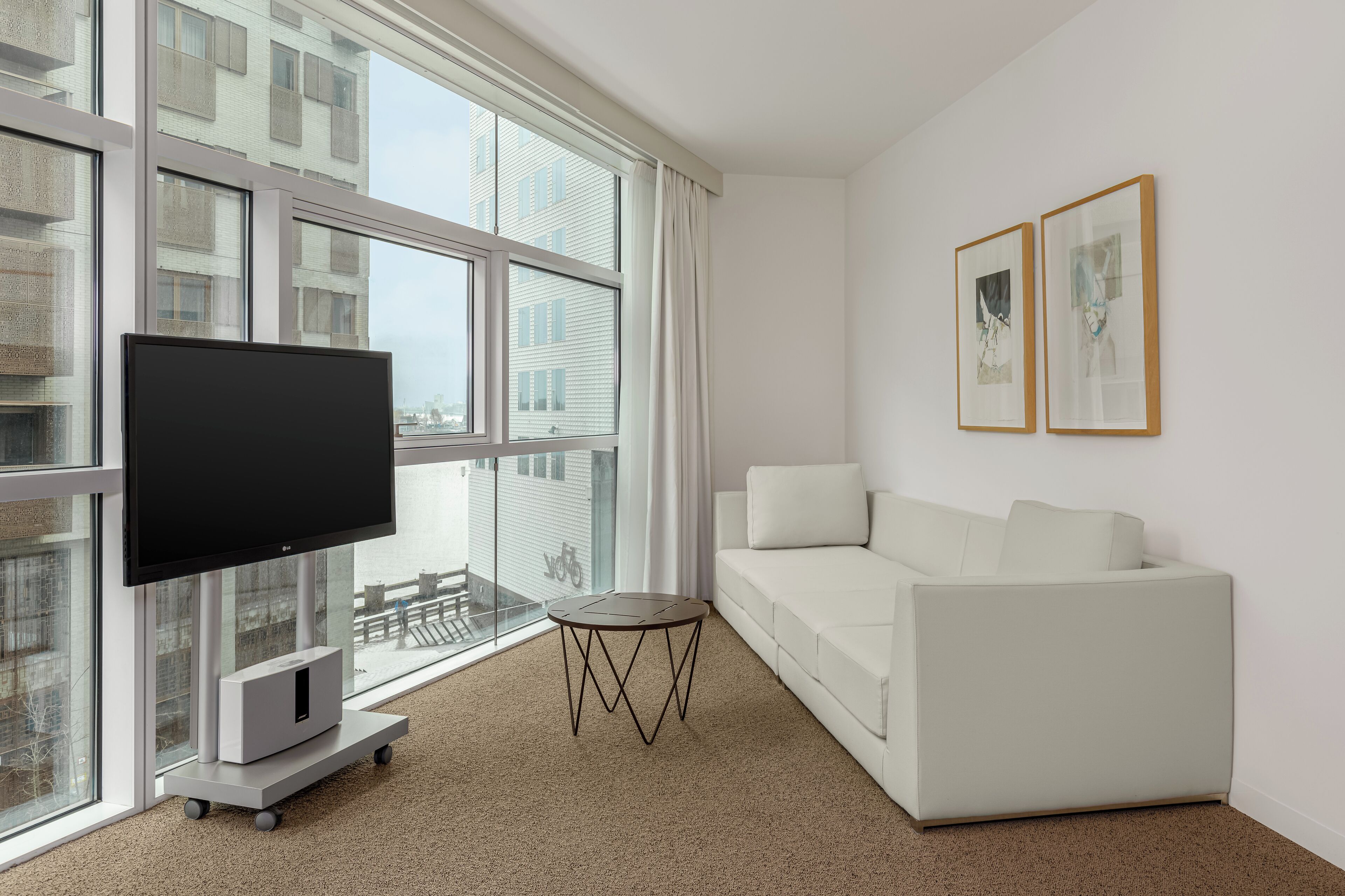 Een moderne woonkamer met een grote flatscreen televisie op een standaard, een witte bank en een kleine ronde tafel.