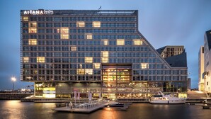 A modern hotel with a glass facade, a dock with a boat, and a waterfront view.