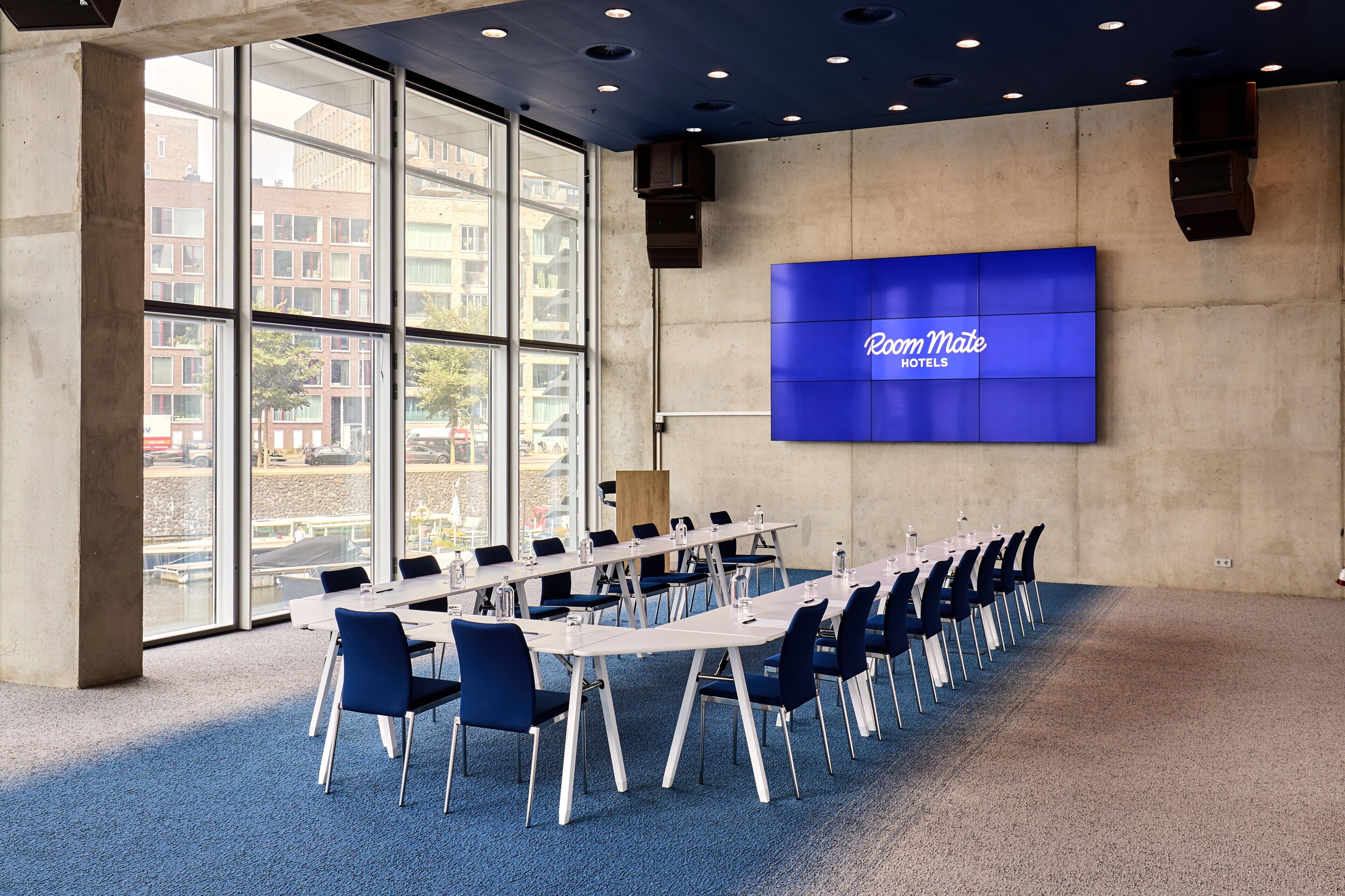 A conference room with a long table, chairs, and a large screen displaying "Room Mate Hotel".