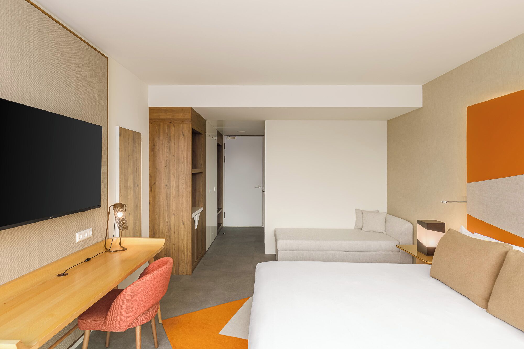 Una habitación de hotel con una cama, un escritorio con silla, televisión y armario.