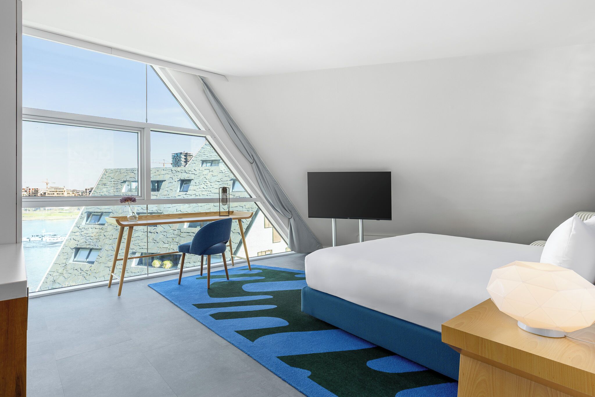 Une chambre d’hôtel moderne dotée d’une grande fenêtre, d’un bureau, d’un lit et d’un téléviseur à écran plat.
