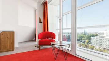 A modern room with a red chair, a small round table, and a large window offering a city view.