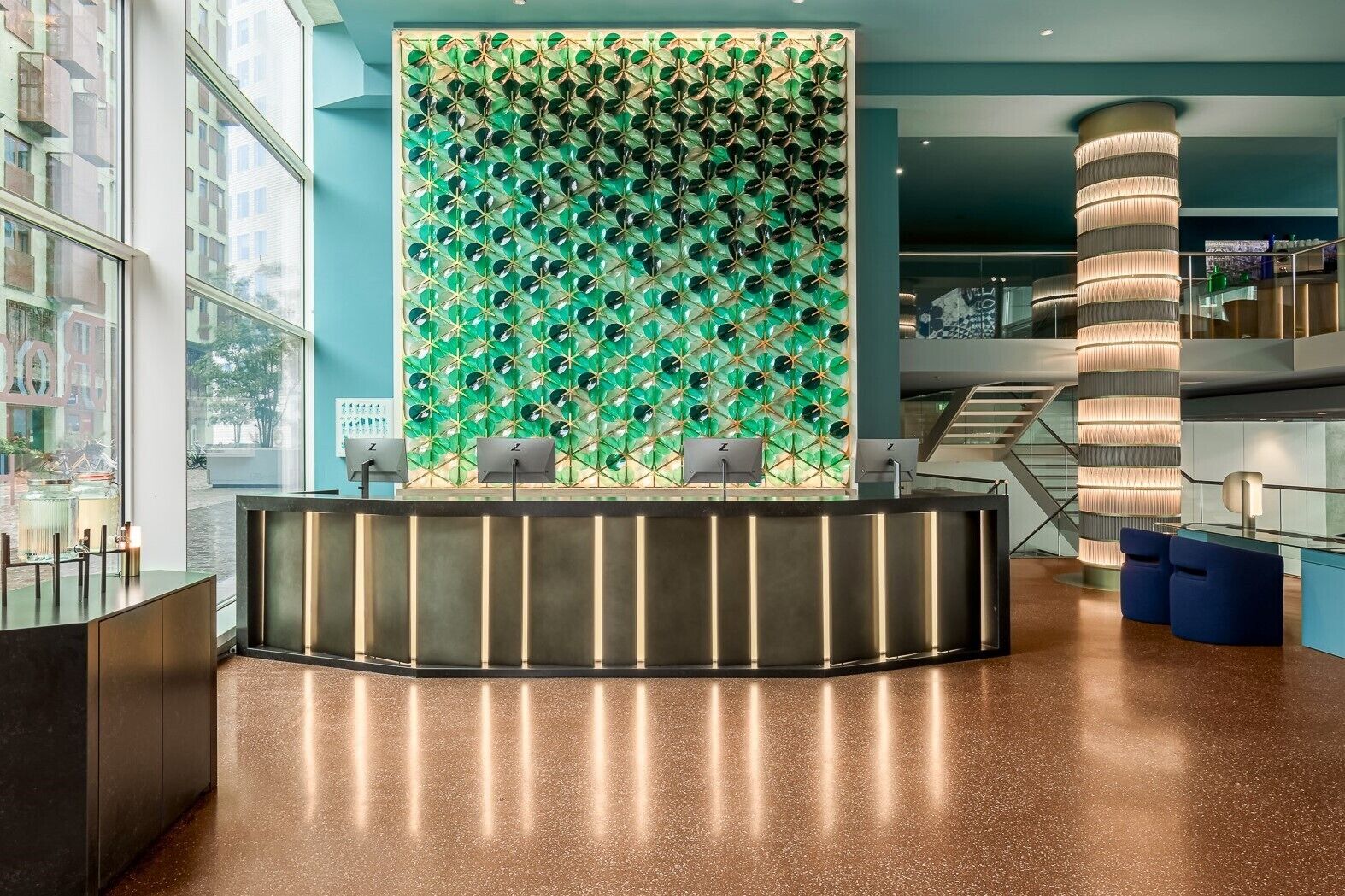 A modern reception area with a green patterned wall, a curved reception desk, and a spiral staircase in the background.