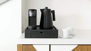 A coffee maker, a kettle, and two white cups on a white countertop with wooden cabinet doors.