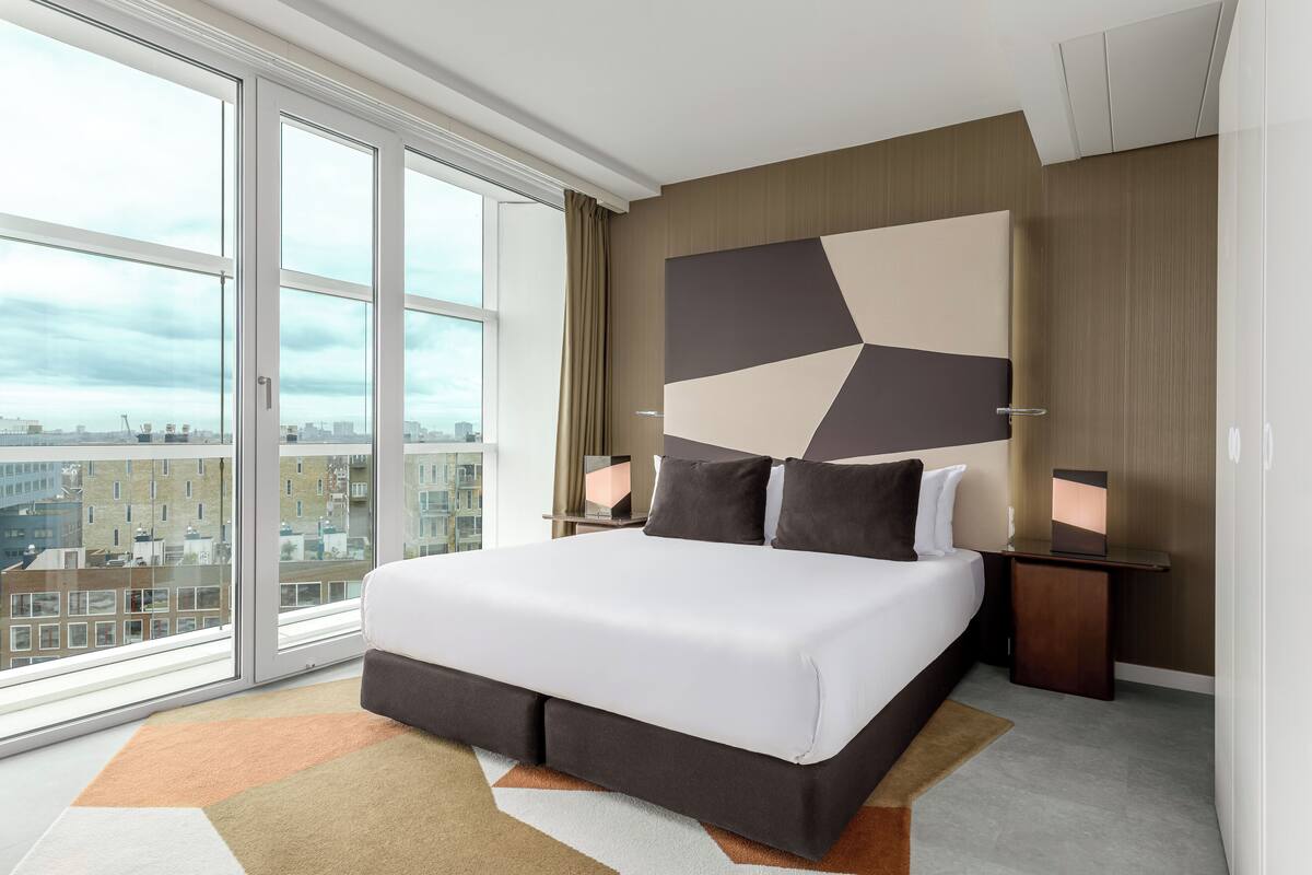 Una habitación de hotel moderna con una cama grande, vistas a la ciudad y un diseño de pared geométrico.