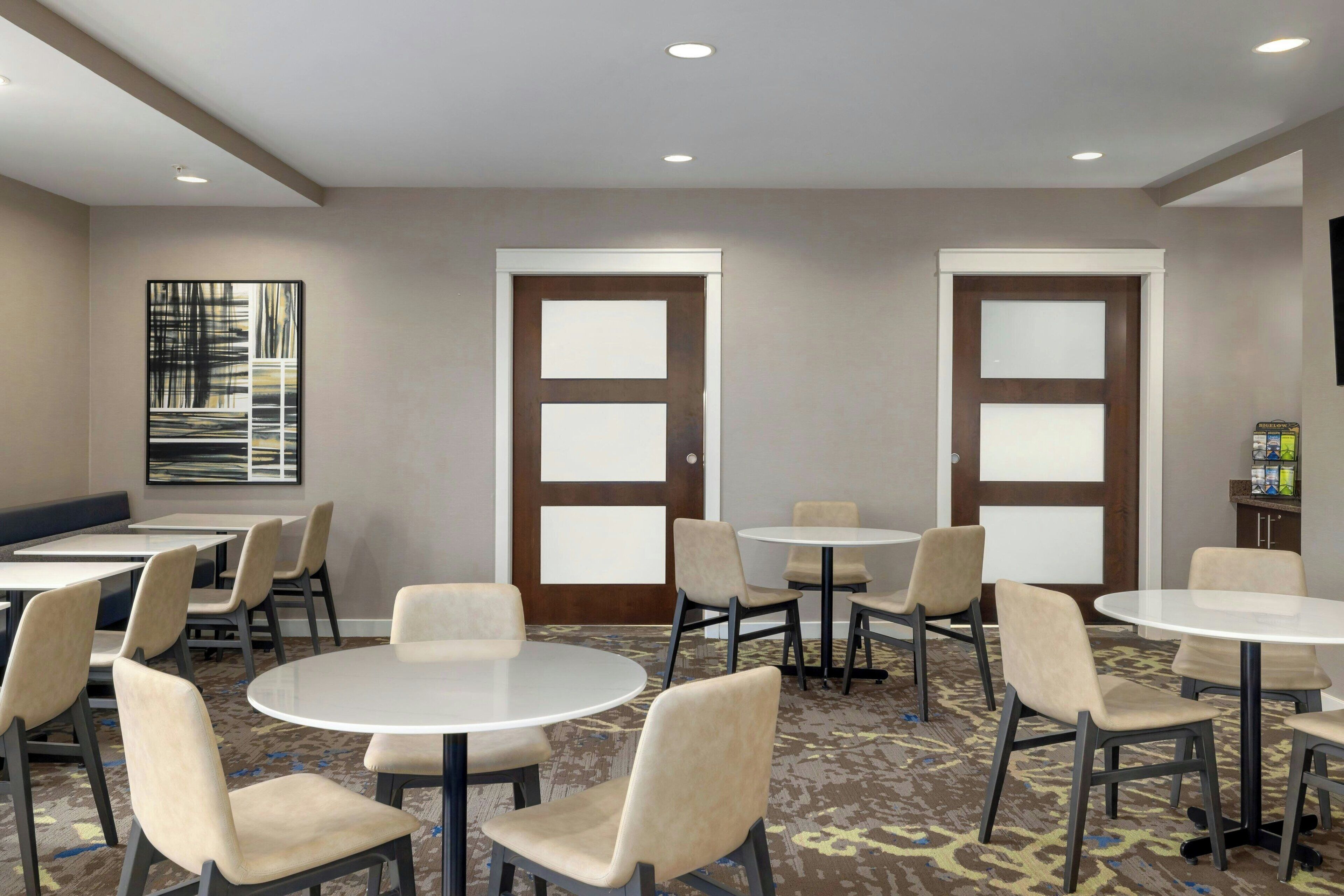A conference room with round tables and chairs, two doors, and a carpeted floor.