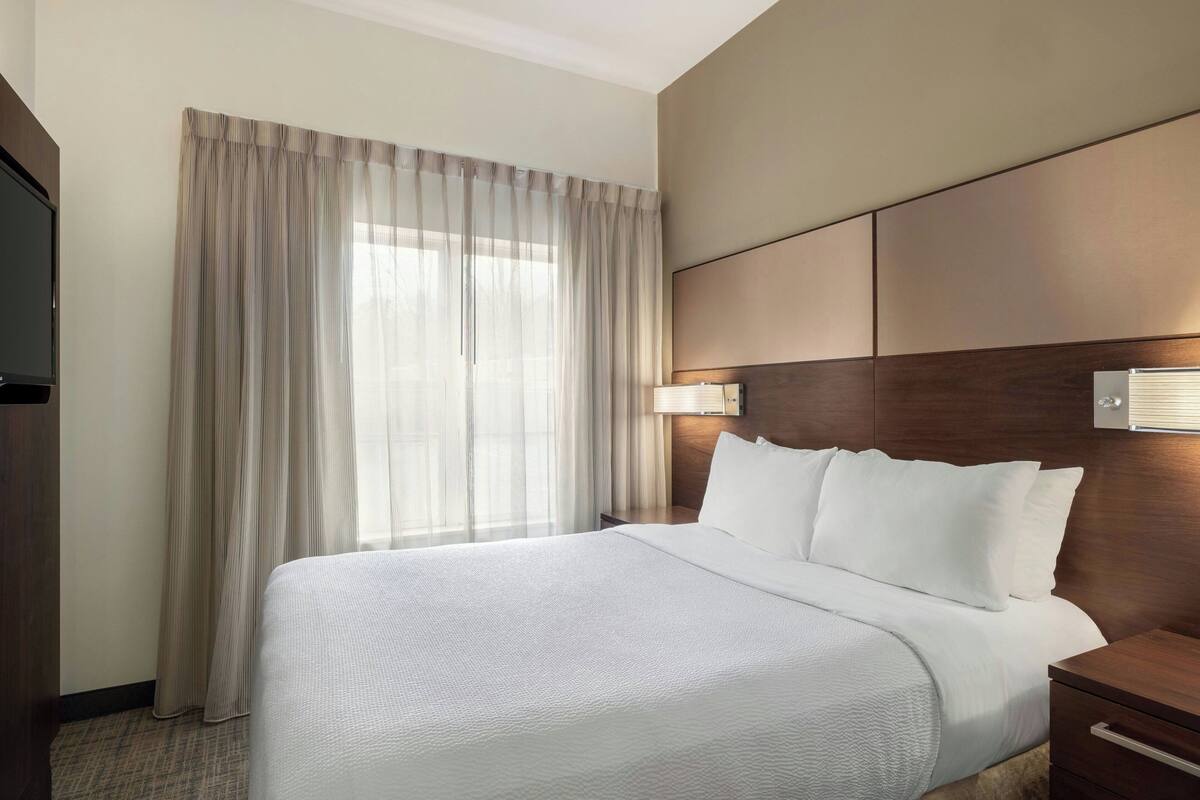 Una habitación de hotel con una cama grande, una mesita de noche, una lámpara y un televisor.