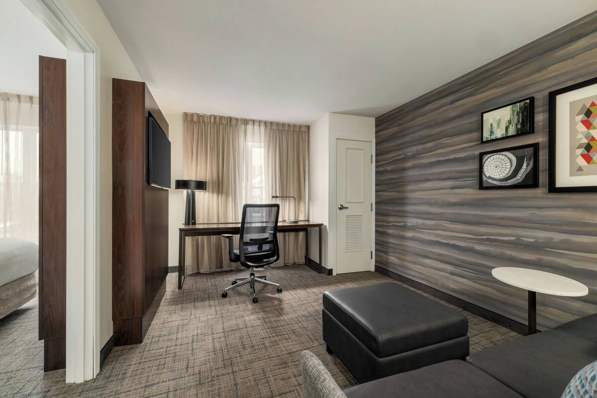 Habitación de hotel con cama, escritorio con silla, una mesita y un sofá.