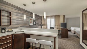 Une chambre d’hôtel moderne dotée d’un coin cuisine, d’une table à manger avec des tabourets de bar, d’une télévision et d’un lit.