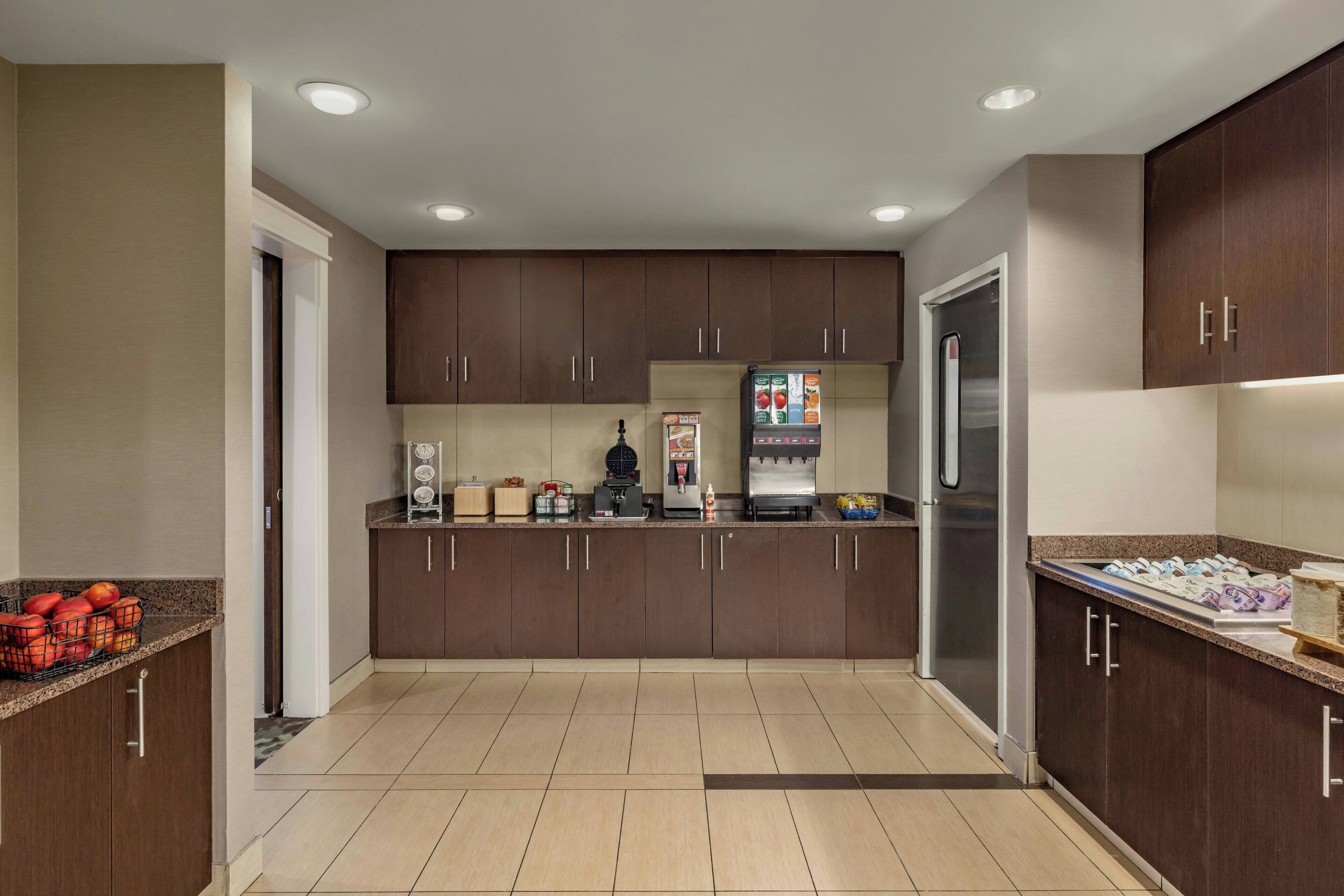 A modern kitchen with dark wood cabinets, a stainless steel refrigerator, and a coffee machine.