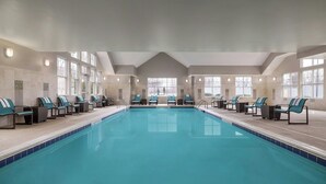 Une grande piscine intérieure dotée de nombreuses chaises longues et d’un plafond très haut.