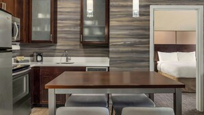 Une cuisine moderne avec des meubles en bois foncé, un réfrigérateur en acier inoxydable et un plan de travail blanc. On y trouve une table à manger avec quatre chaises et des luminaires suspendus au-dessus.