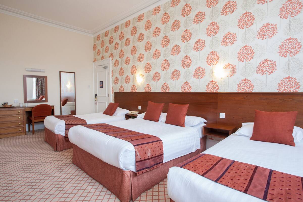 A hotel room with three beds, a desk, and a chair.