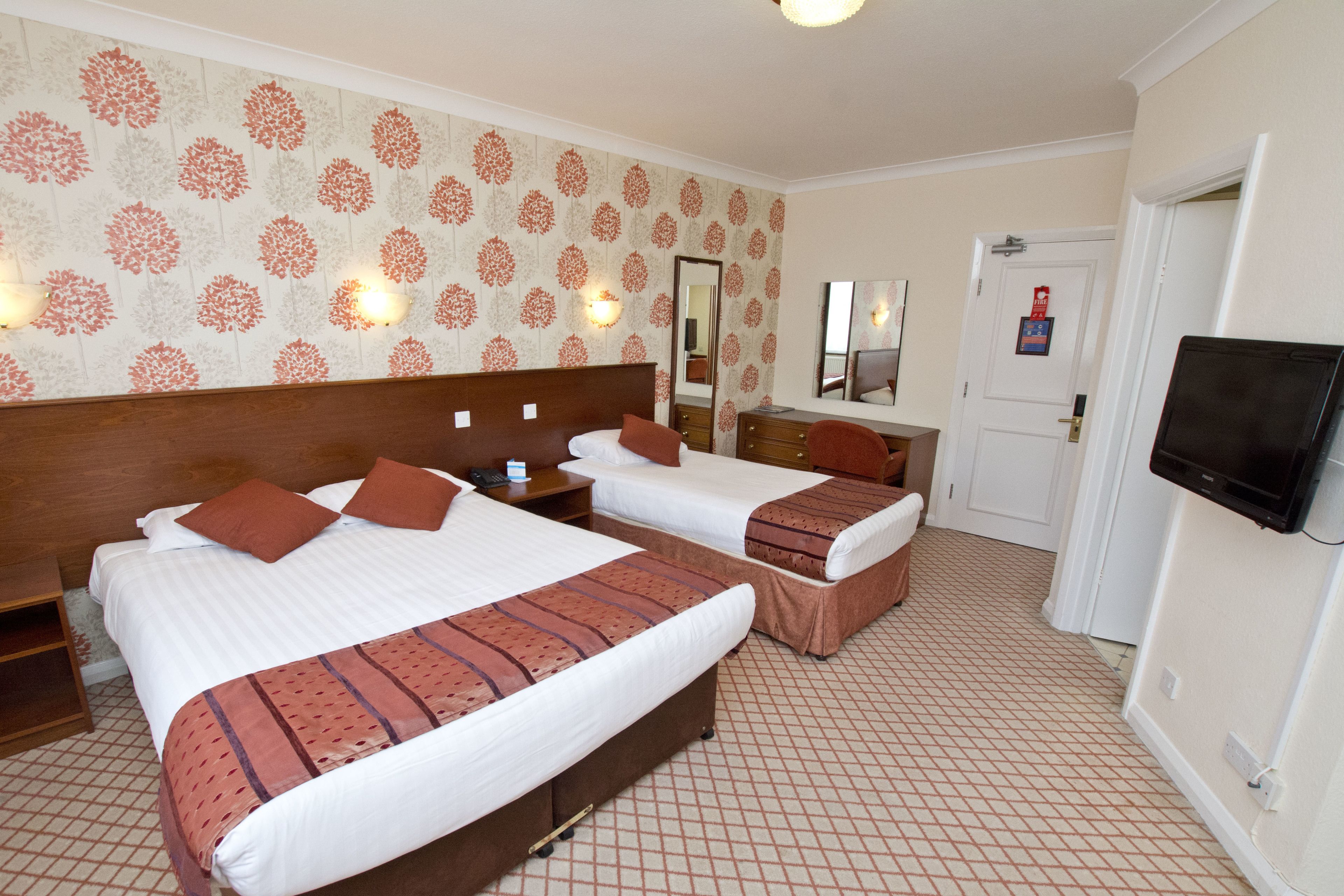 A hotel room with two beds, a TV, a mirror, and a door.