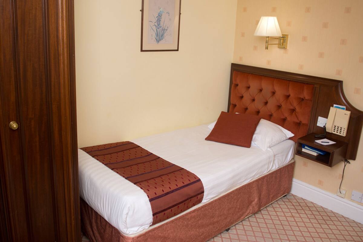 A neatly made bed with a brown headboard, a bedside lamp, and a telephone on a nightstand.