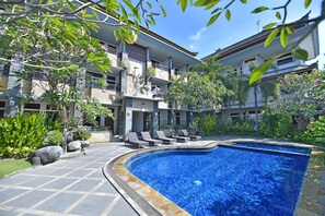 A swimming pool with a tiled edge, surrounded by lounge chairs and potted plants. - Sandat Hotel Kuta (Kuta)