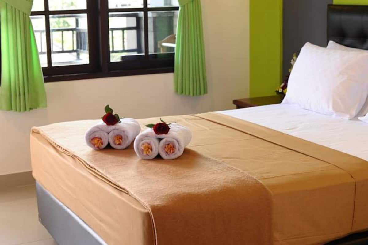 A neatly made bed with a brown bedspread, two rolled towels with flowers, and white pillows.