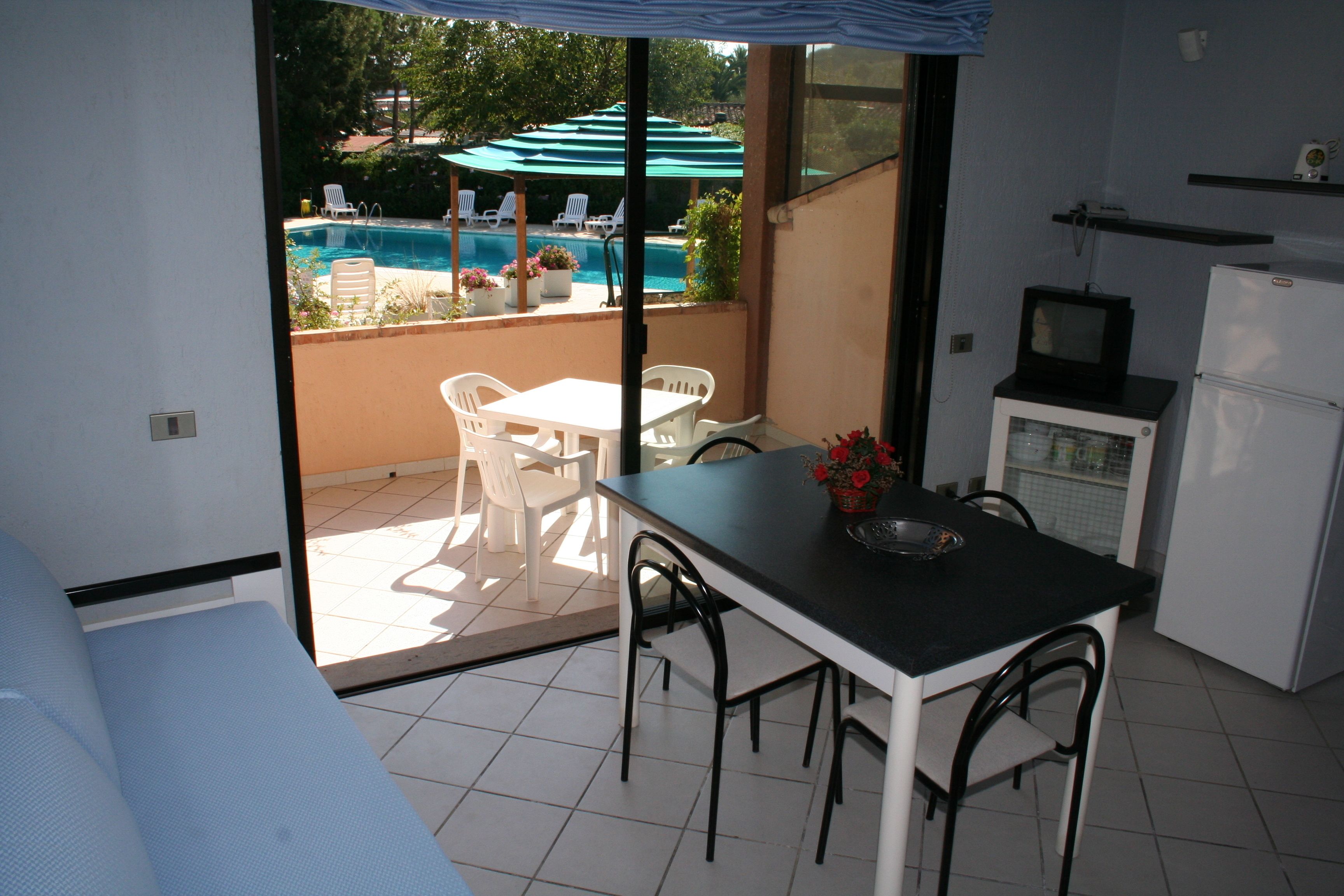 A room with a dining table, chairs, a TV, and a refrigerator.