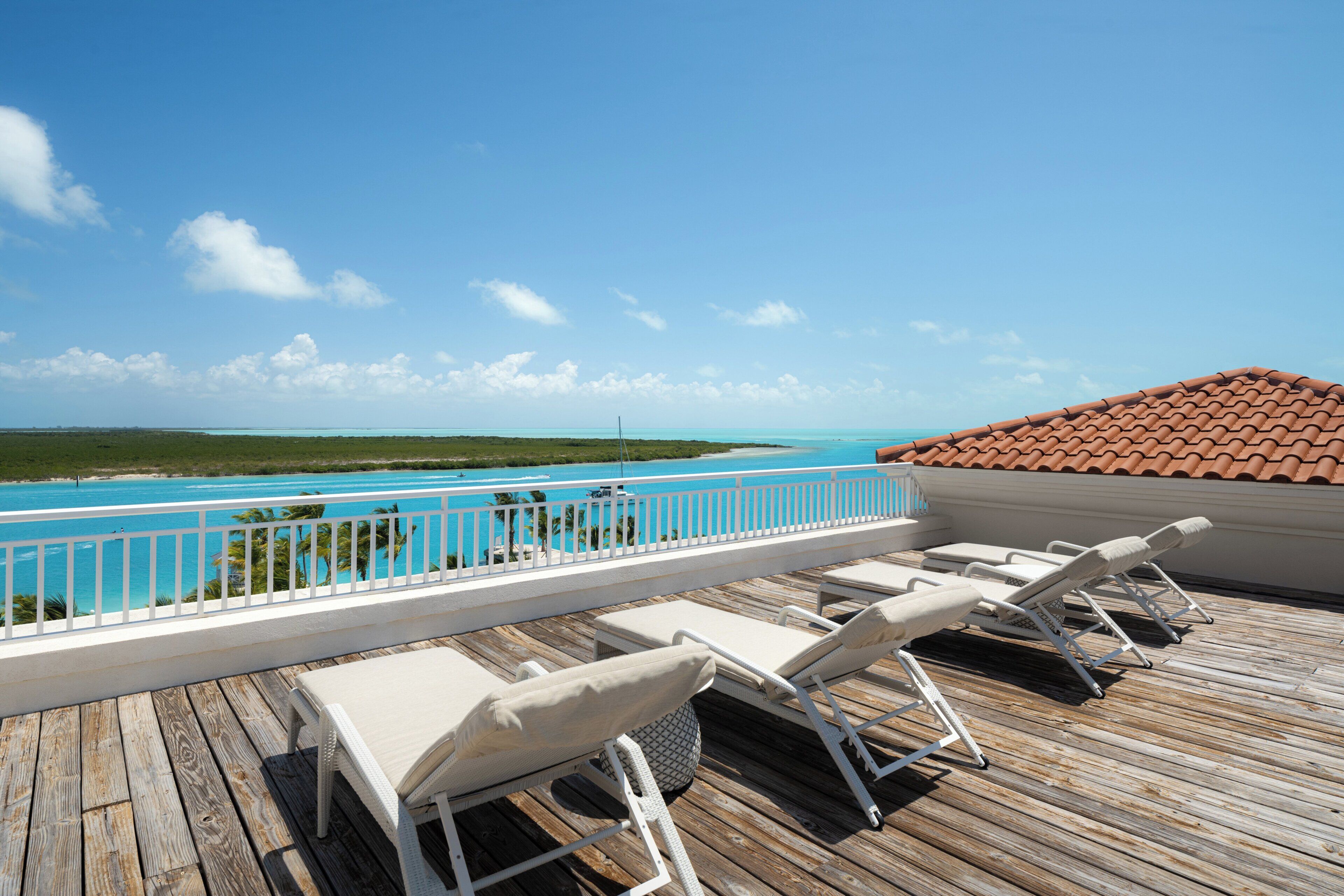 Een houten terras met lounge fauteuils en uitzicht op een turquoise zee.