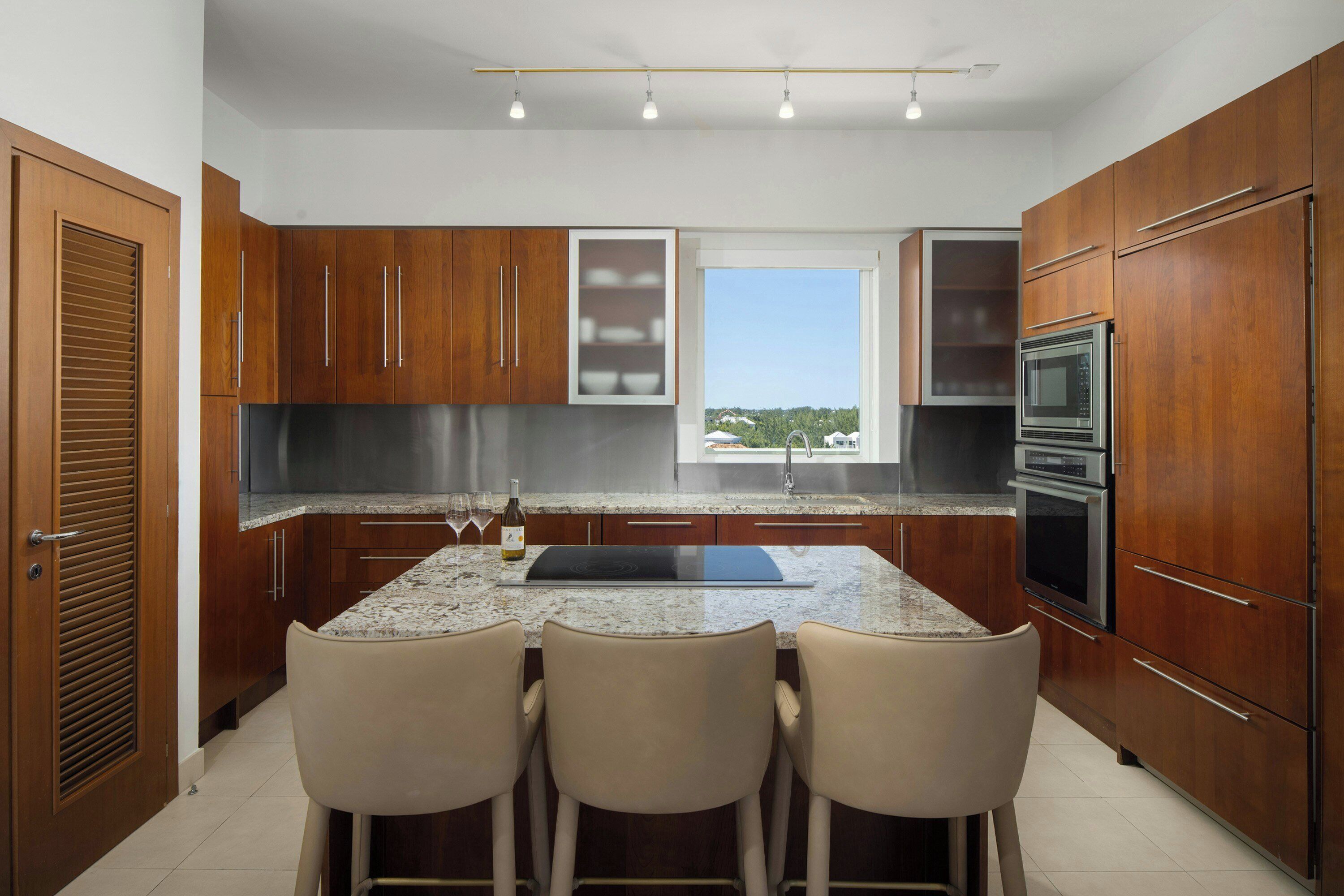 A modern kitchen with wooden cabinets, a granite countertop, a built-in oven, and a window overlooking greenery.