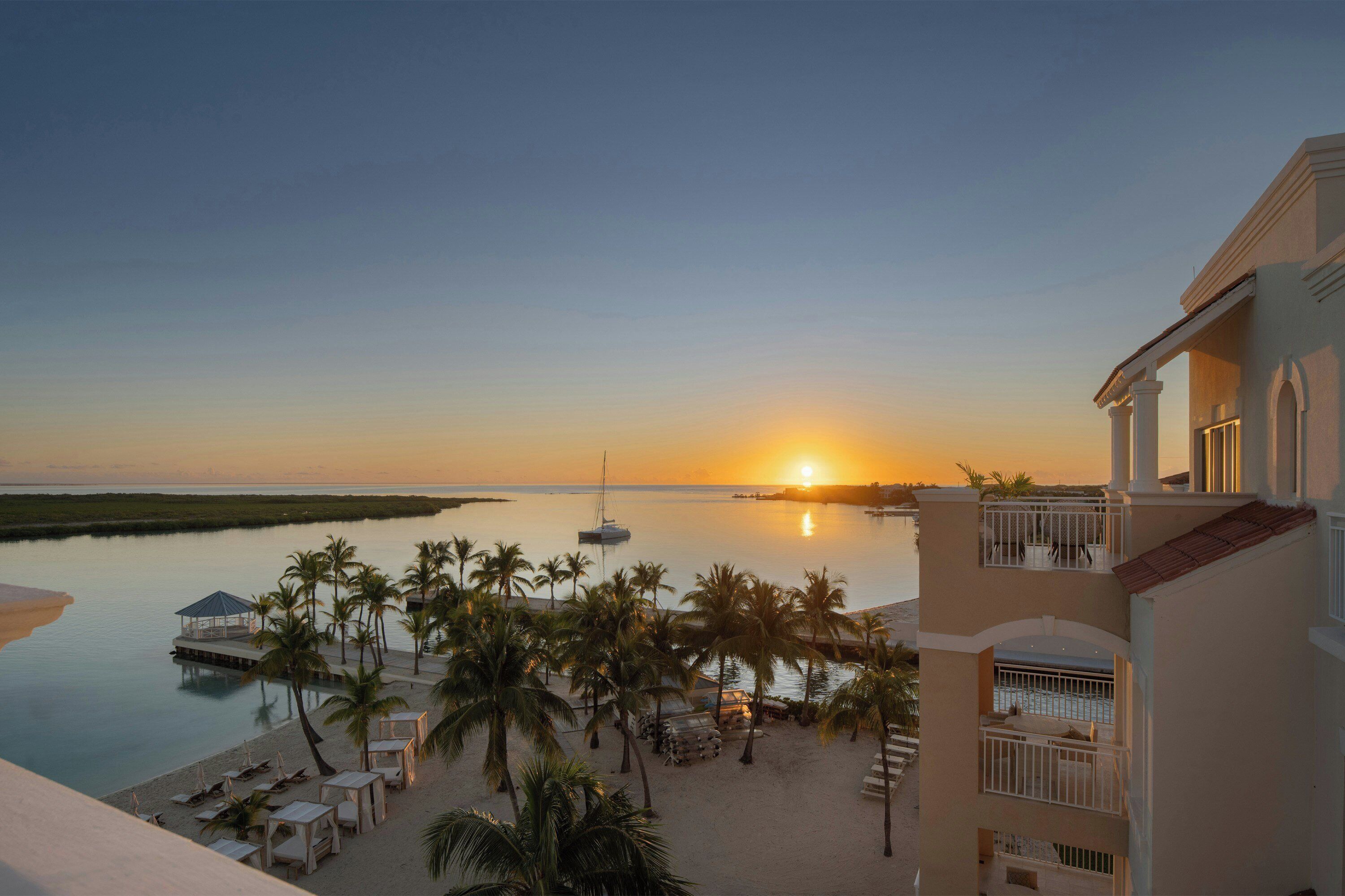 Ein Strandhotel mit Sonnenuntergangsblick, Palmen und einer Anlegestelle mit einem Boot.