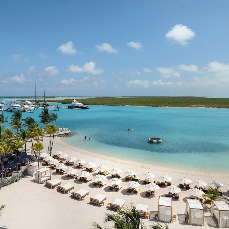 A beach resort with a marina, sun loungers, umbrellas, and a clear view of the ocean.