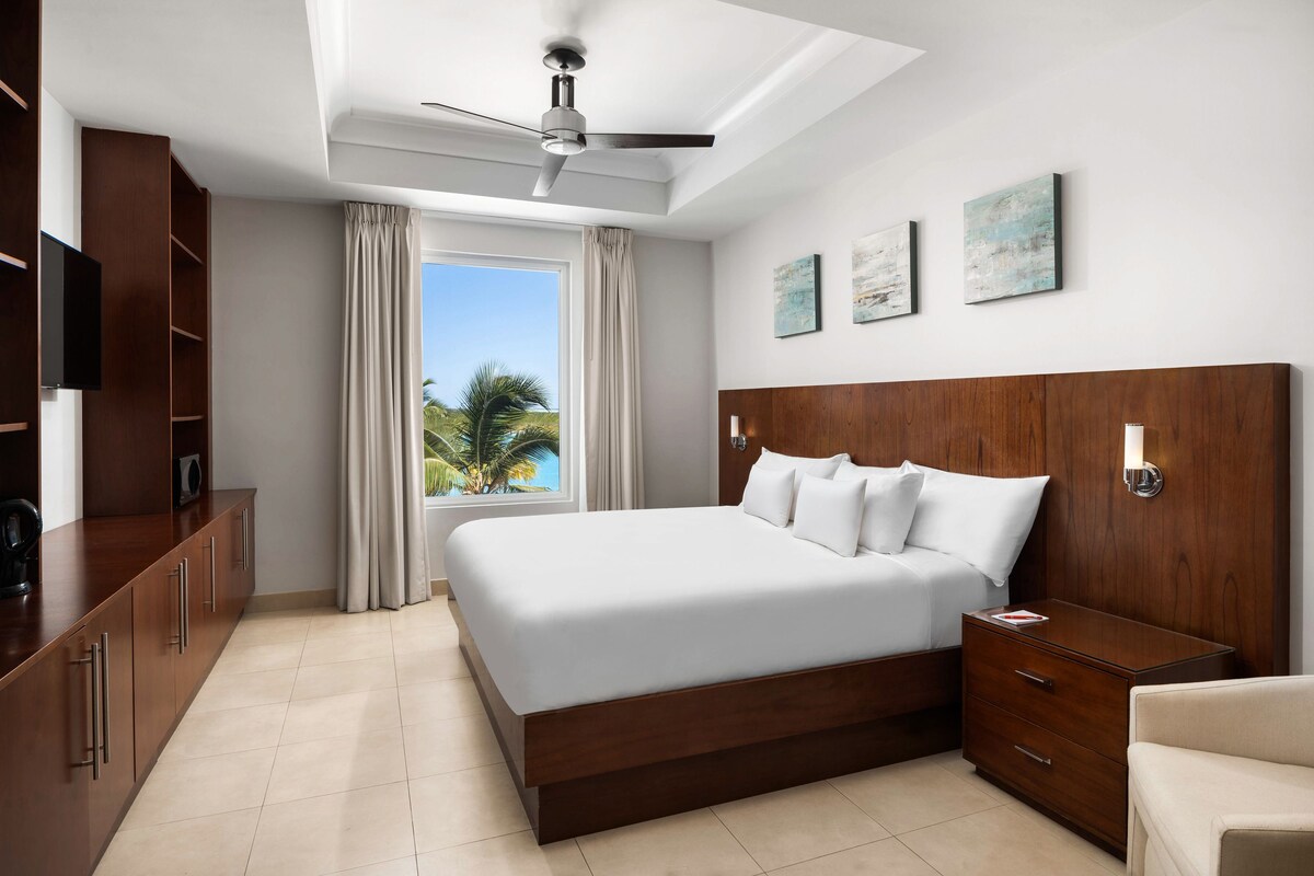 A modern hotel room with a large bed, wooden headboard, a bedside table, a wardrobe, and a ceiling fan.