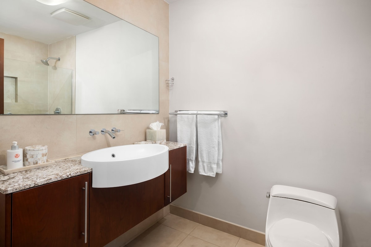 Een badkamer met een witte wasbak, een grote spiegel, een douche en een toilet.