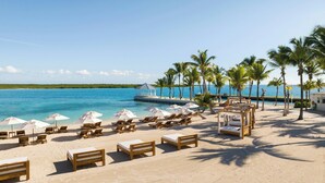 Een strand met ligbedden, parasols en een houten constructie aan het water.